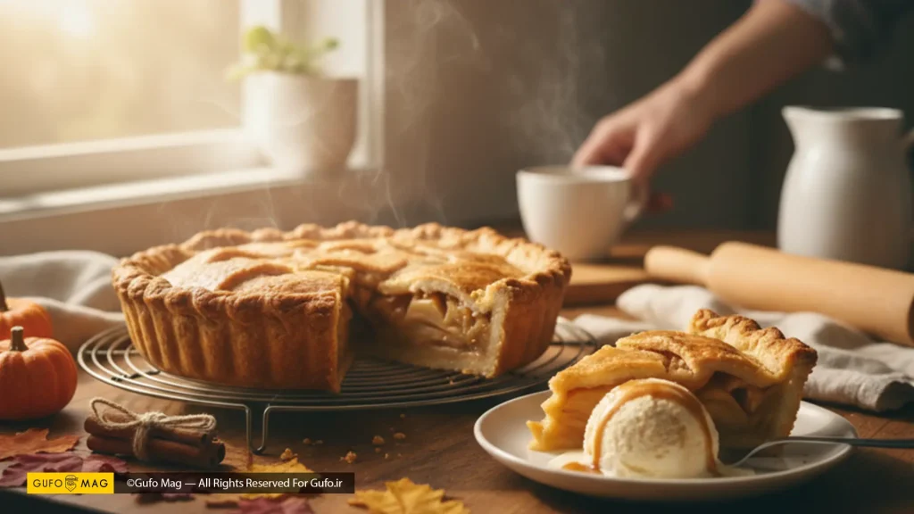 یک پای سیب گرم با یک برش جدا شده، همراه با بستنی وانیلی، برگهای پاییزی و کدو تنبلهای تزئینی، و فردی با فنجان