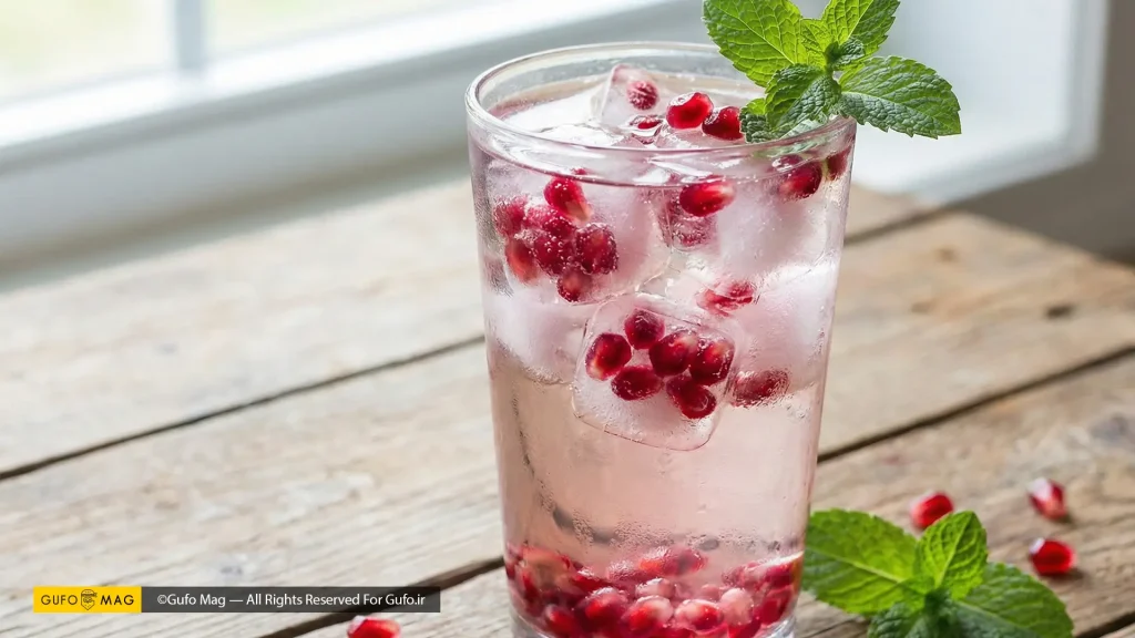 لیوان نوشیدنی خنک با تکههای یخ تزیینی حاوی دانههای انار قرمز